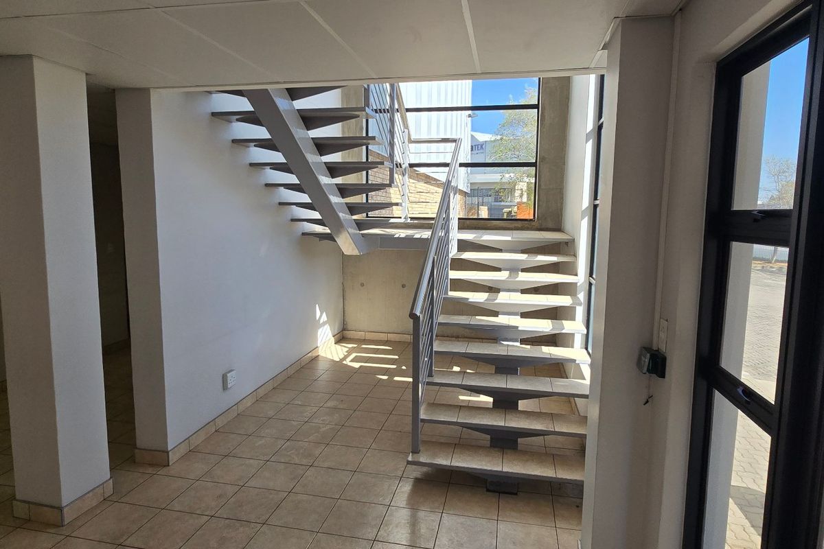 Bright industrial entrance foyer featuring a modern metal staircase, tiled flooring, and large windows providing ample natural light.