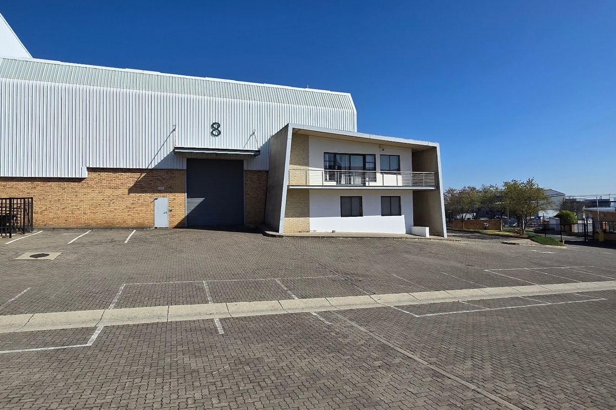 Industrial property featuring a large roller shutter door, brick and metal cladding facade, and a paved parking area with a small balcony.