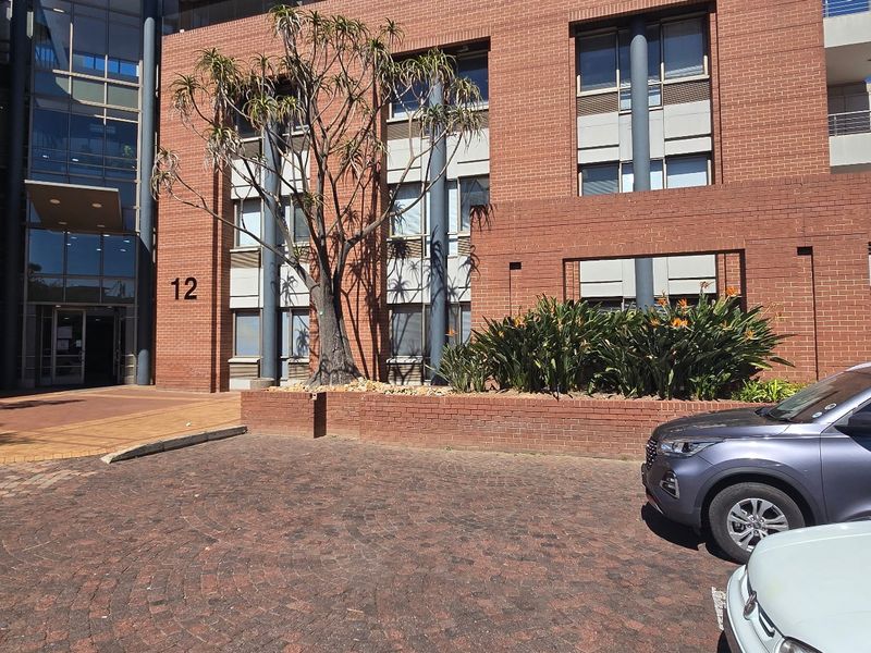 Front exterior view of a commercial office building featuring a brick facade, glass entrance, and paved parking area.