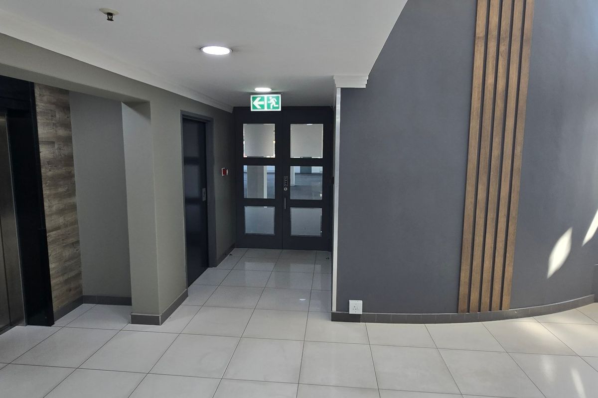 Modern commercial hallway featuring tiled flooring, elevator access, decorative wall paneling, and clear emergency exit signage.