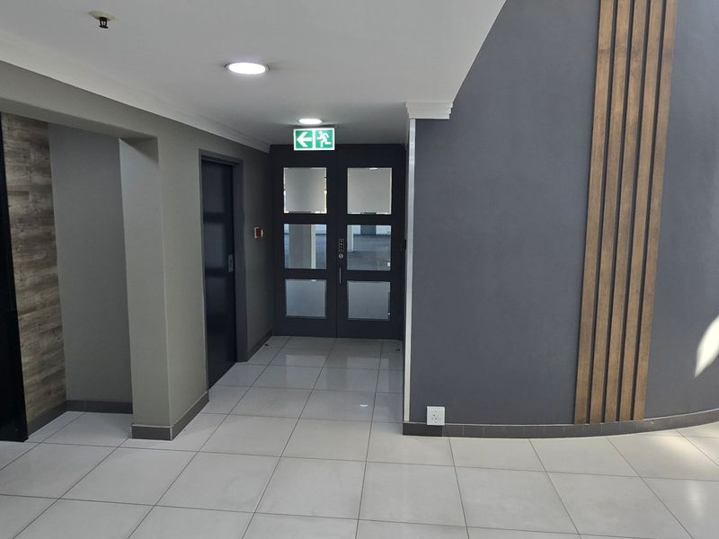 Modern commercial hallway featuring tiled flooring, elevator access, decorative wall paneling, and clear emergency exit signage.