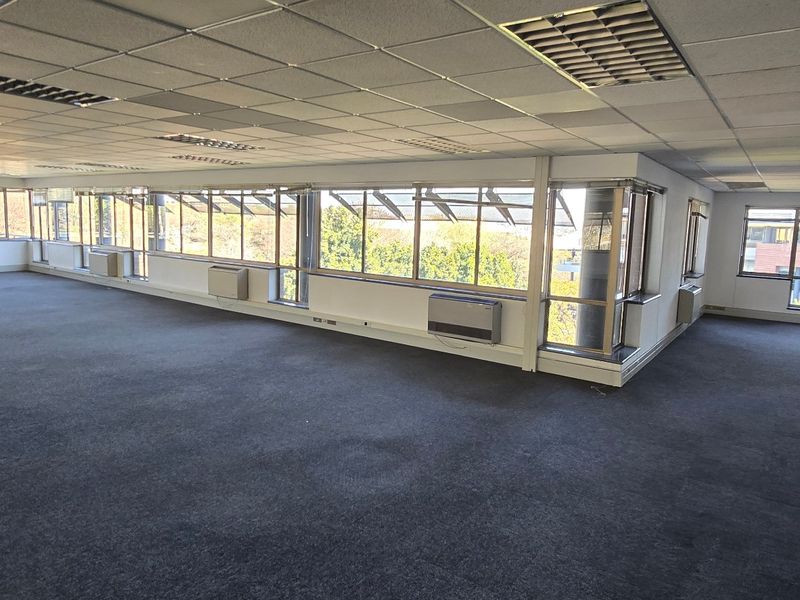 Spacious open-plan commercial office area featuring large windows, suspended ceilings, and wall-mounted air conditioning units, offering a versatile workspace with natural light.