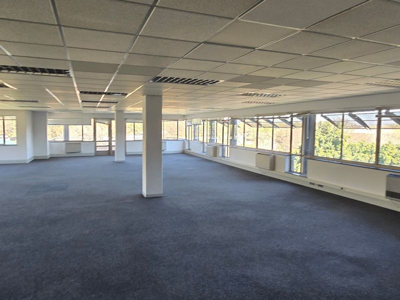 Spacious open-plan commercial office area featuring large windows, suspended ceilings, and integrated HVAC units, offering a versatile workspace with ample natural light.