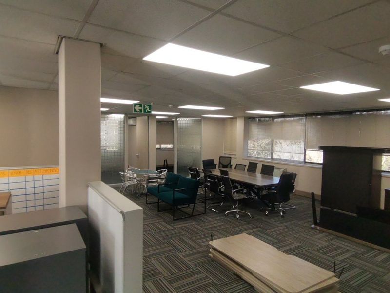 A functional commercial office space featuring suspended ceilings, recessed lighting, carpet tiles, and glass partition walls, suitable for a professional work environment.