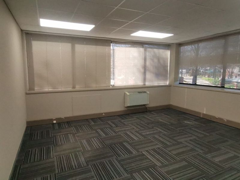 A vacant commercial office space featuring a suspended ceiling, recessed lighting, carpet tile flooring, and an integrated HVAC unit with large windows.