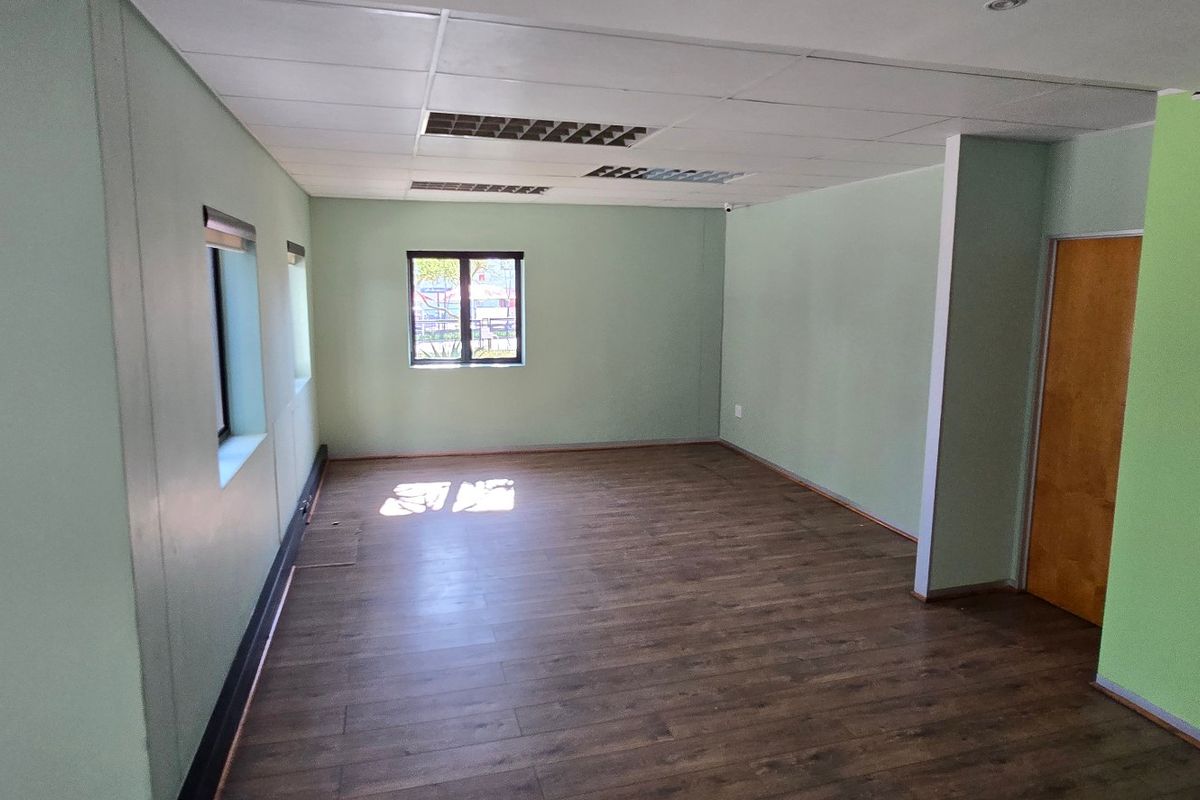 A vacant commercial office space featuring laminate flooring, a drop ceiling with recessed lighting, and painted walls.
