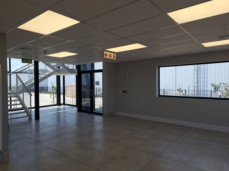 Modern industrial entrance lobby featuring tiled flooring, a sleek metal staircase, and ample natural light through large glass panels.