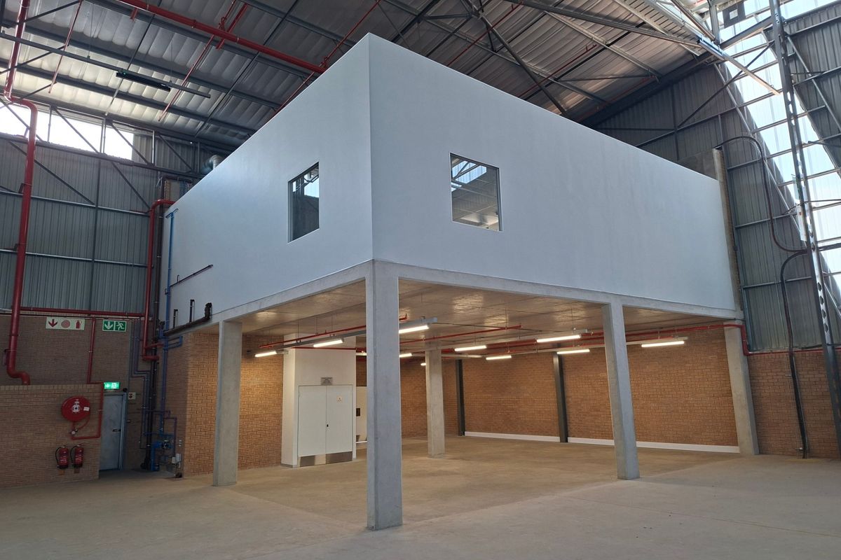 Spacious industrial warehouse interior featuring a concrete mezzanine level, exposed steel roof structure, fire suppression systems, and durable concrete flooring.