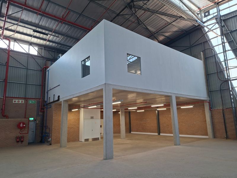 Spacious industrial warehouse interior featuring a concrete mezzanine level, exposed steel roof structure, fire suppression systems, and durable concrete flooring.