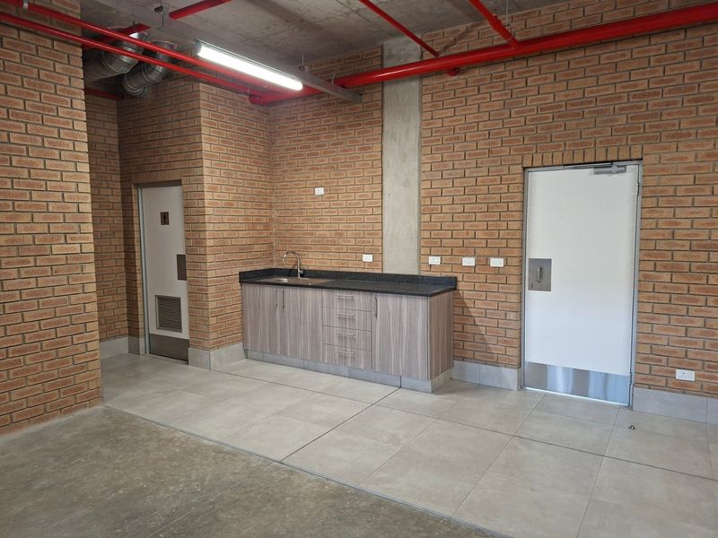 Industrial utility space featuring exposed brickwork, high-visibility fire sprinkler systems, tiled flooring, and a functional kitchenette area with stone countertops.