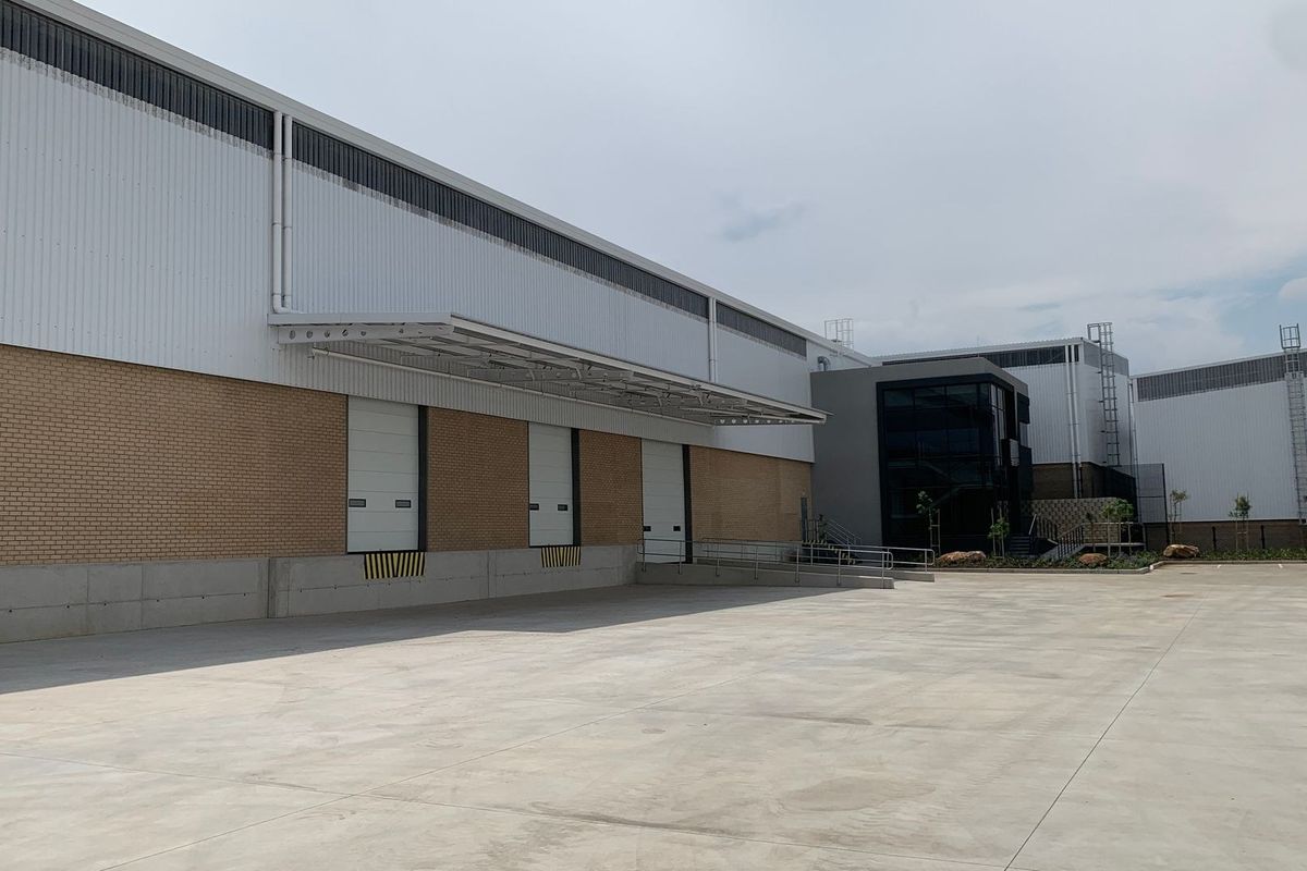 Industrial warehouse exterior featuring multiple loading docks with roller shutter doors, a large concrete yard, and modern metal and brick facade construction.