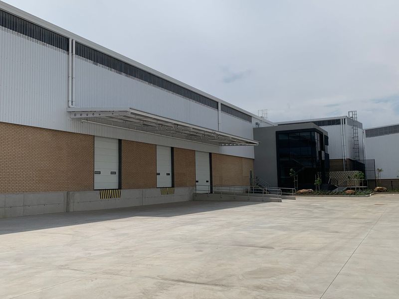 Industrial warehouse exterior featuring multiple loading docks with roller shutter doors, a large concrete yard, and modern metal and brick facade construction.