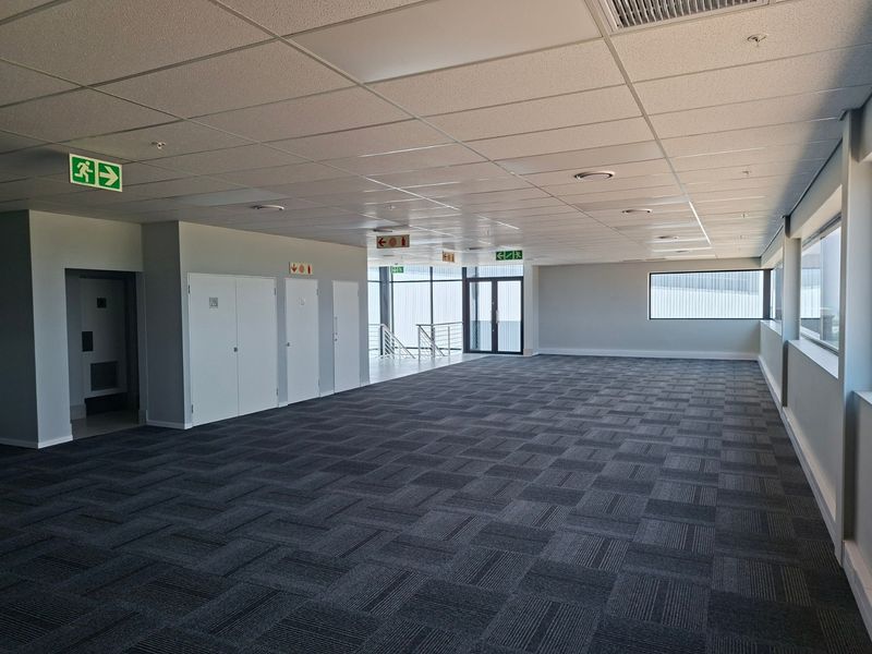 A spacious, open-plan industrial office area featuring a suspended ceiling, recessed lighting, and durable carpet tiles, offering a clean and professional workspace.