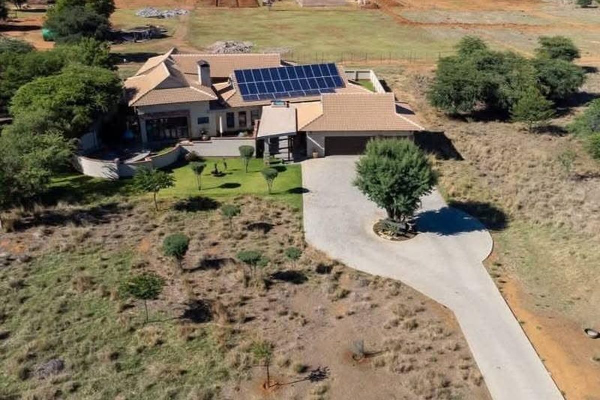 Aerial view of a residential property featuring a tiled roof with integrated solar panels, a concrete driveway, and a landscaped garden area.