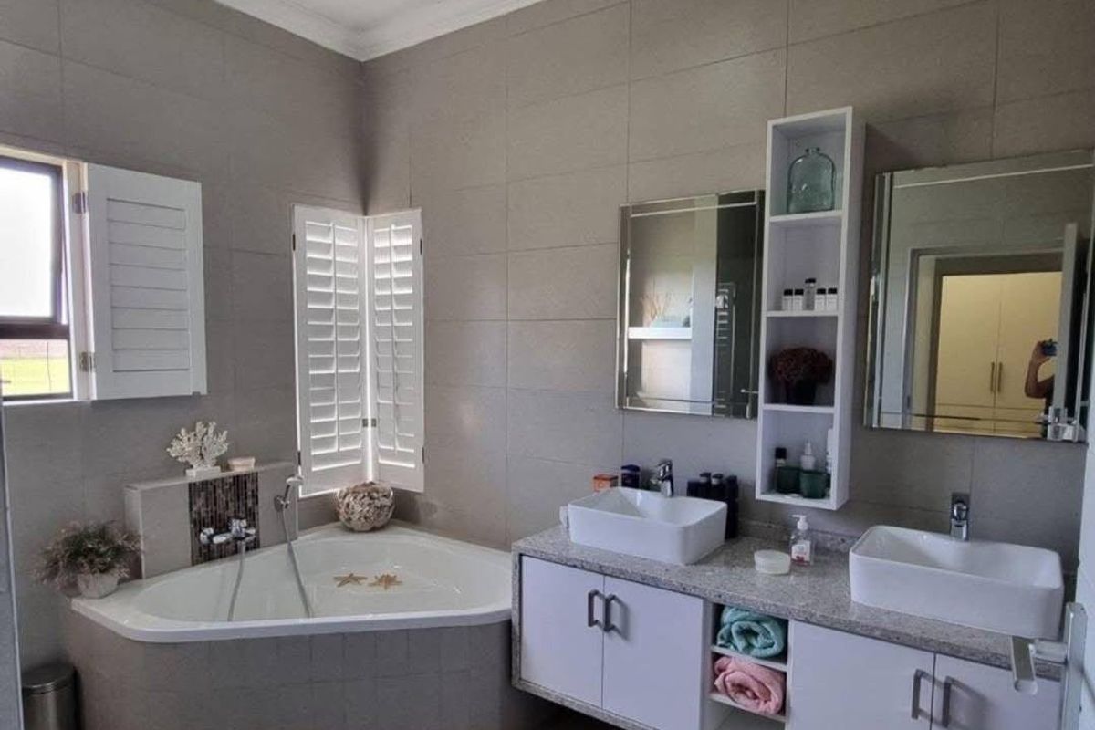 Modern bathroom featuring a corner bathtub, double vanity with vessel sinks, granite countertops, and plantation shutters for natural light control.