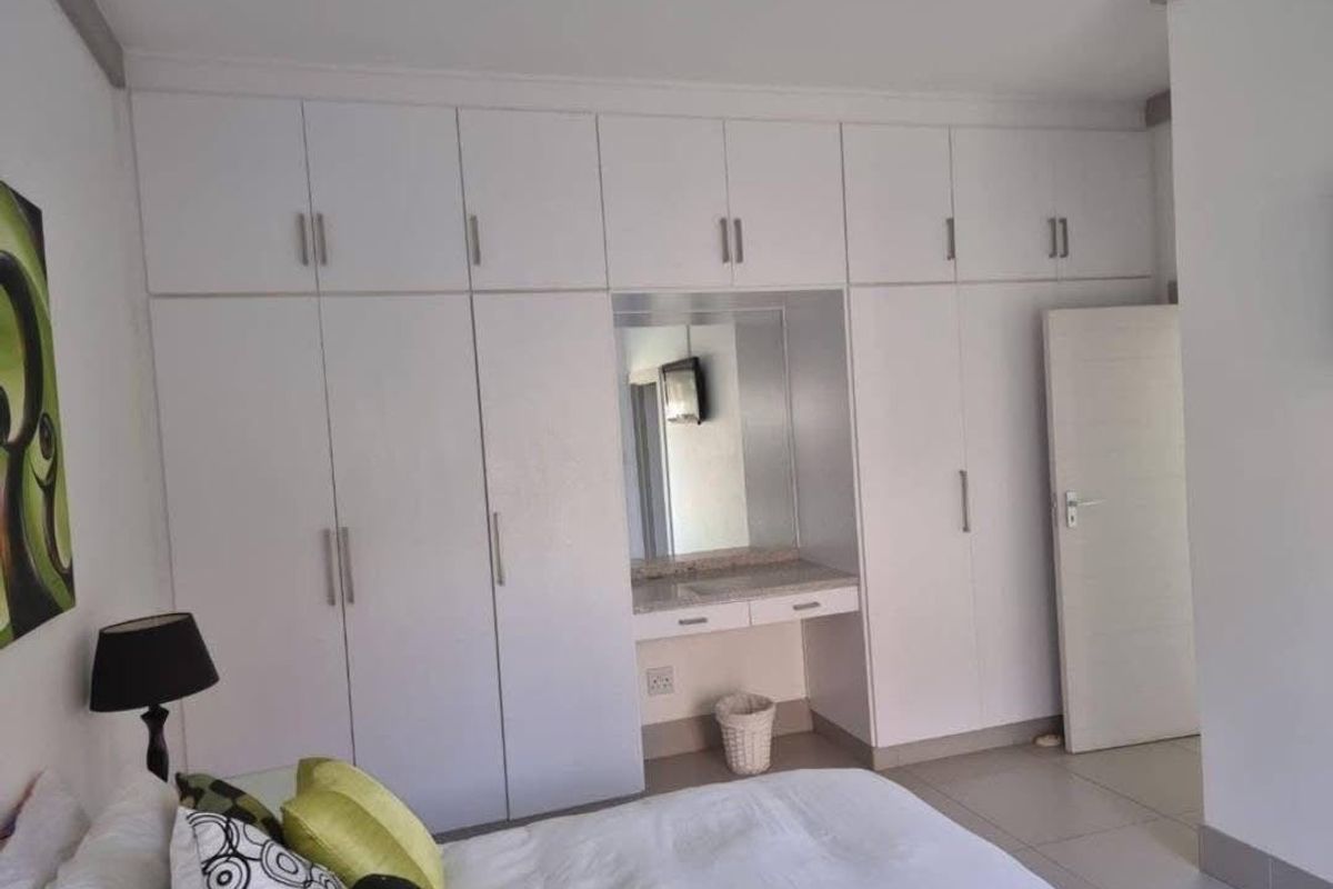Bedroom featuring extensive white built-in cupboards with an integrated vanity station and neutral tiled flooring.