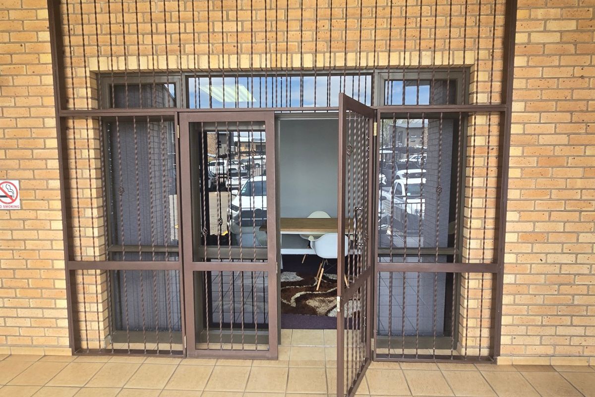 Commercial building entrance featuring a brick facade, tiled flooring, and secure metal gate access.