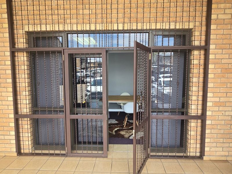 Commercial building entrance featuring a brick facade, tiled flooring, and secure metal gate access.