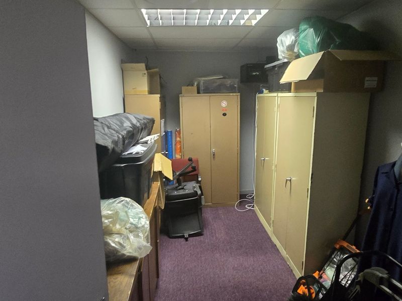 A small utility or storage room featuring a suspended ceiling with recessed lighting and carpeted flooring.