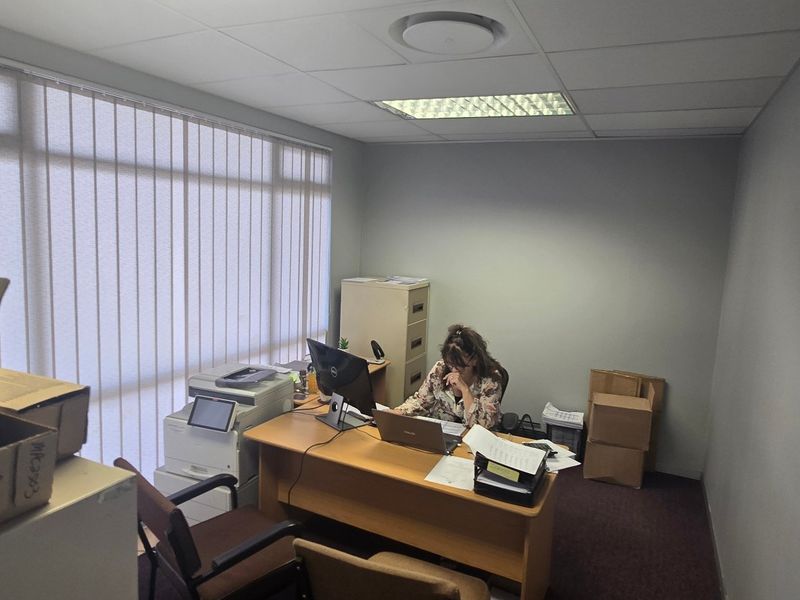 A functional commercial office space featuring a suspended ceiling, recessed lighting, and large windows with vertical blinds.