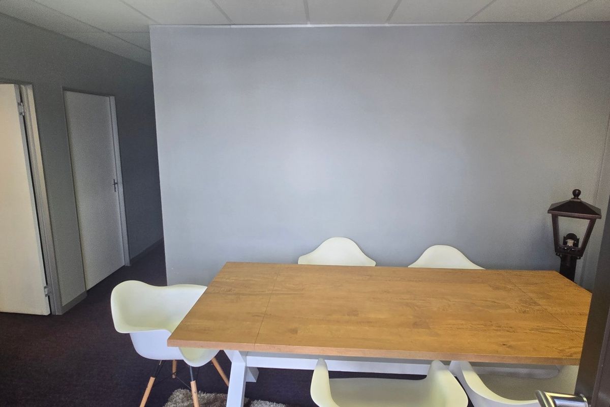 A functional office space featuring neutral grey walls, suspended ceiling tiles, and carpeted flooring, suitable for a professional work environment.