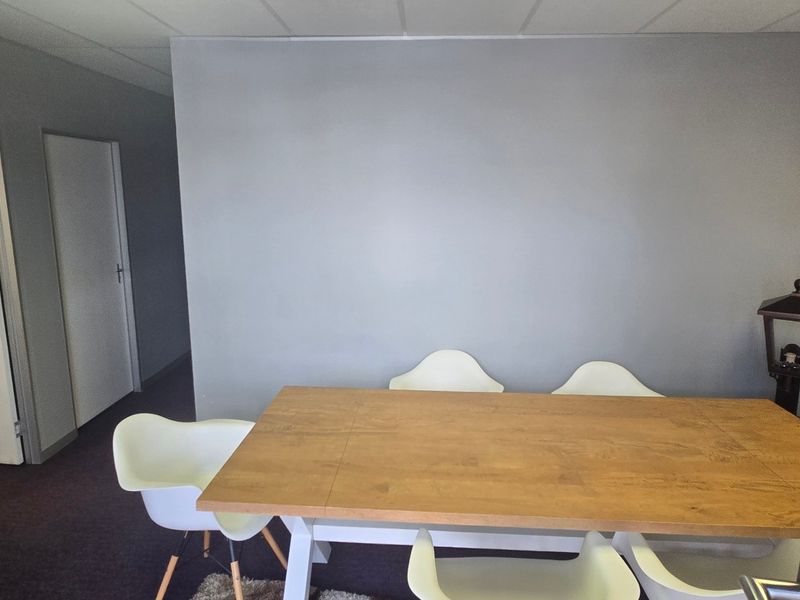 A functional office space featuring neutral grey walls, suspended ceiling tiles, and carpeted flooring, suitable for a professional work environment.