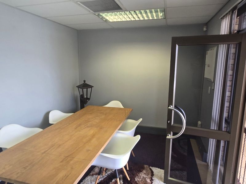 A functional office space featuring a suspended ceiling with recessed lighting and an aluminium-framed glass entrance door.