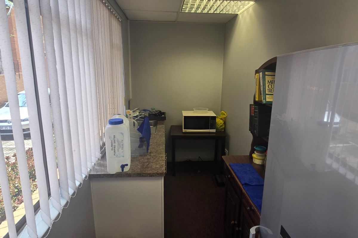 A compact commercial kitchenette area featuring a laminate countertop, vertical blinds, and a drop ceiling, suitable for office staff use.
