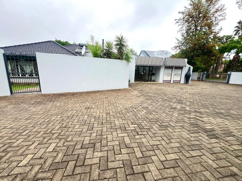 Front exterior view of a commercial property featuring a paved driveway, boundary wall, and entrance with striped awnings and signage.