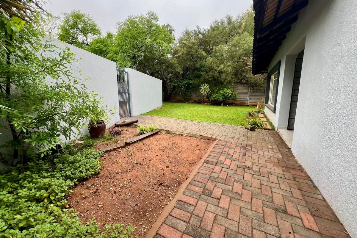 A rear exterior view featuring a paved patio area, a small lawn, and a boundary wall with a metal gate.