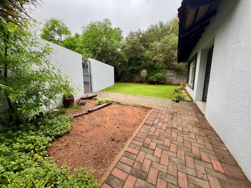 A rear exterior view featuring a paved patio area, a small lawn, and a boundary wall with a metal gate.