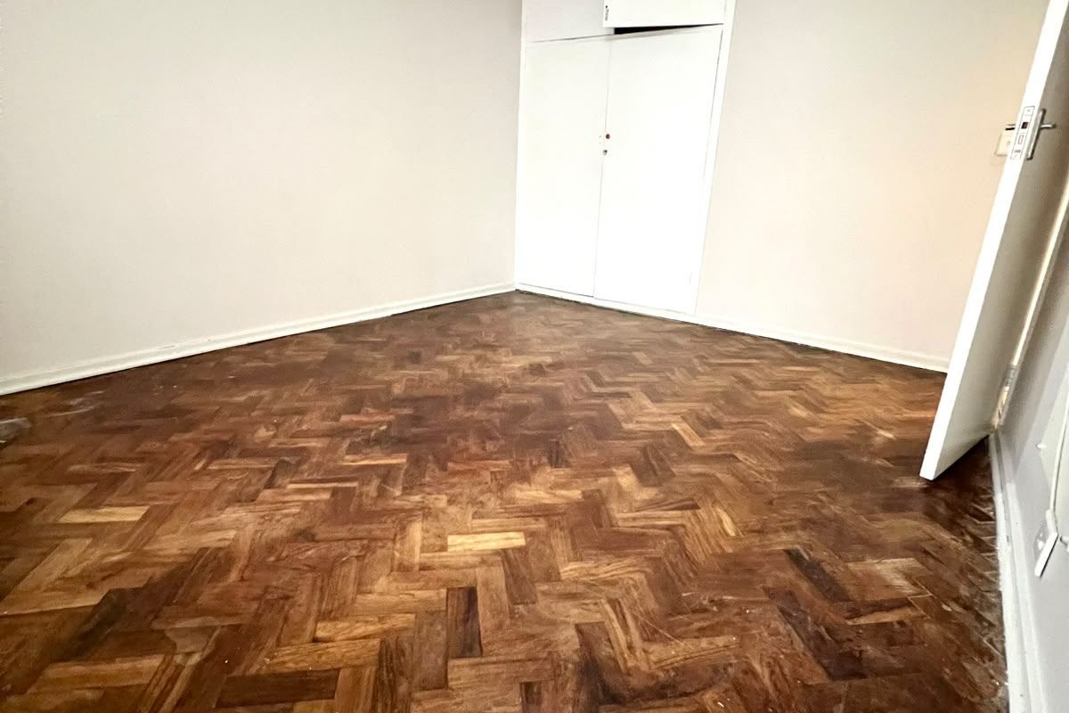 An empty bedroom featuring classic parquet flooring, a built-in cupboard with overhead storage, and neutral wall finishes.