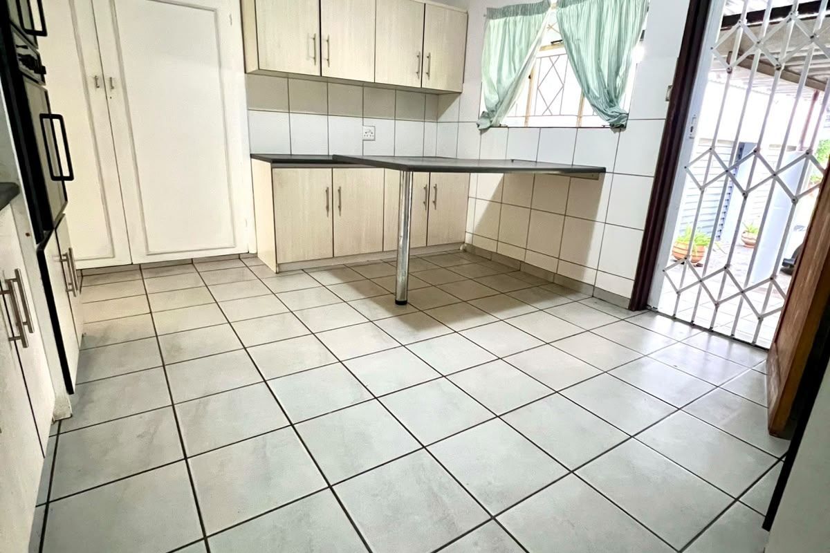 A functional kitchen featuring built-in cabinetry, a breakfast counter, tiled flooring, and direct access to an outdoor area through a security gate.