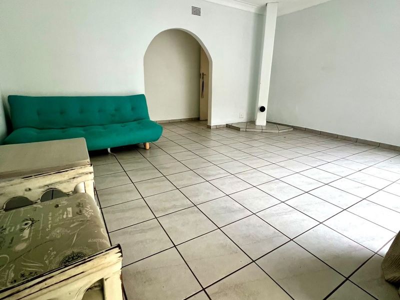 A spacious living area featuring tiled flooring, a ceiling fan, and a distinctive arched doorway leading to an adjacent space.