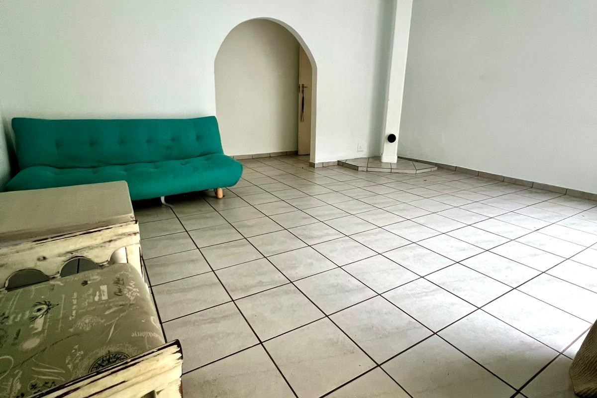 A spacious living area featuring tiled flooring, a ceiling fan, and a distinctive arched doorway leading to an adjacent space.