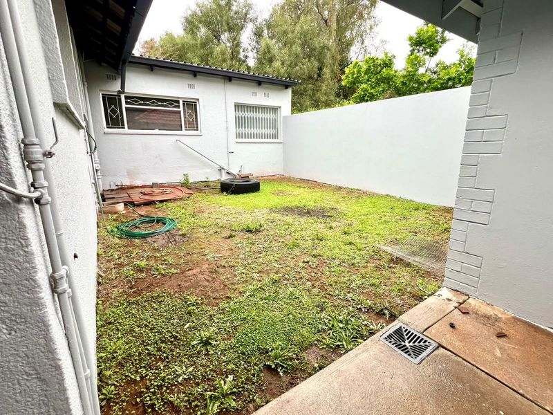 A rear exterior courtyard area featuring a concrete patio, drainage system, and a small garden space enclosed by boundary walls.