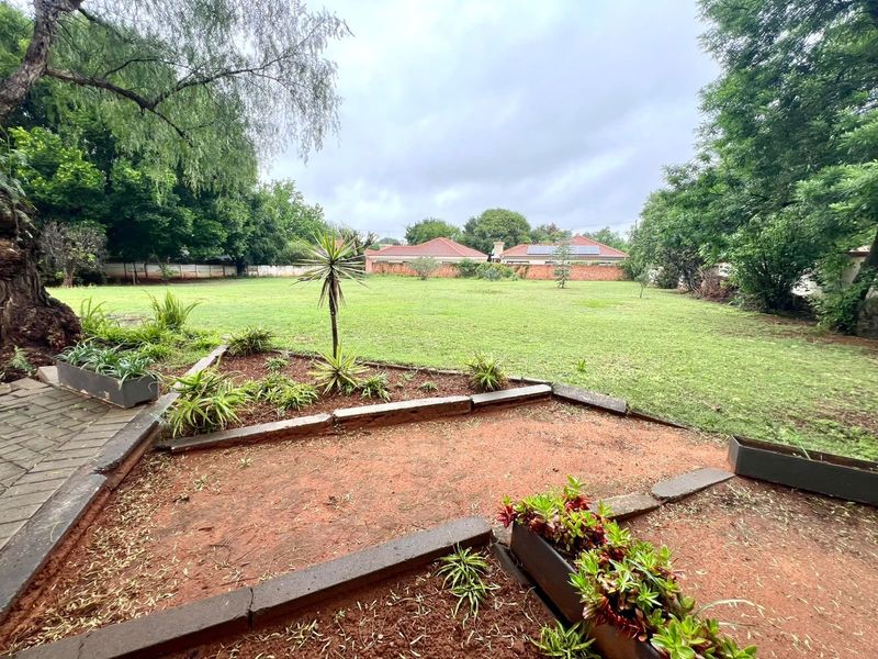 A spacious, well-maintained garden featuring a large lawn, paved walkway, and established perimeter walling, offering a private outdoor space.