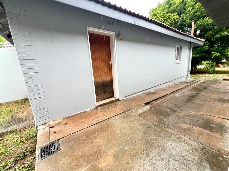 Rear exterior view of the commercial property featuring a paved walkway, drainage system, and a timber access door with visible weathering.
