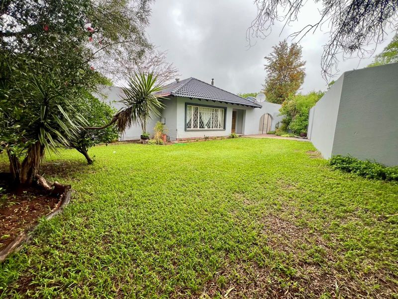 A view of the rear exterior of the property featuring a well-maintained lawn, perimeter wall, and a tiled roof structure.