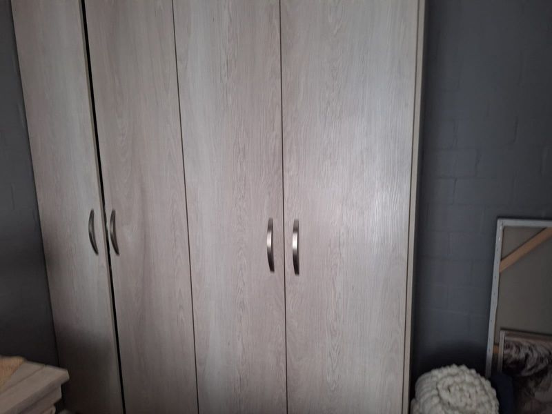 A bedroom featuring a modern light wood-grain built-in wardrobe with metallic handles against a dark grey painted brick wall.