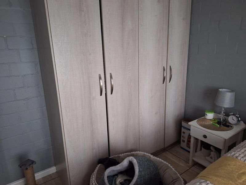 A bedroom featuring a light wood-finish built-in wardrobe and painted exposed brick walls.