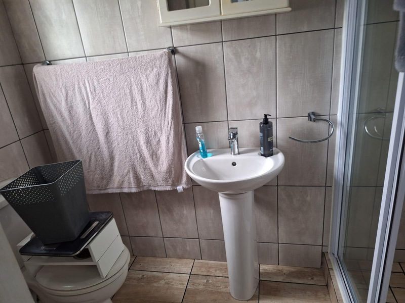 A functional bathroom featuring a pedestal basin, tiled walls and flooring, and a shower enclosure.