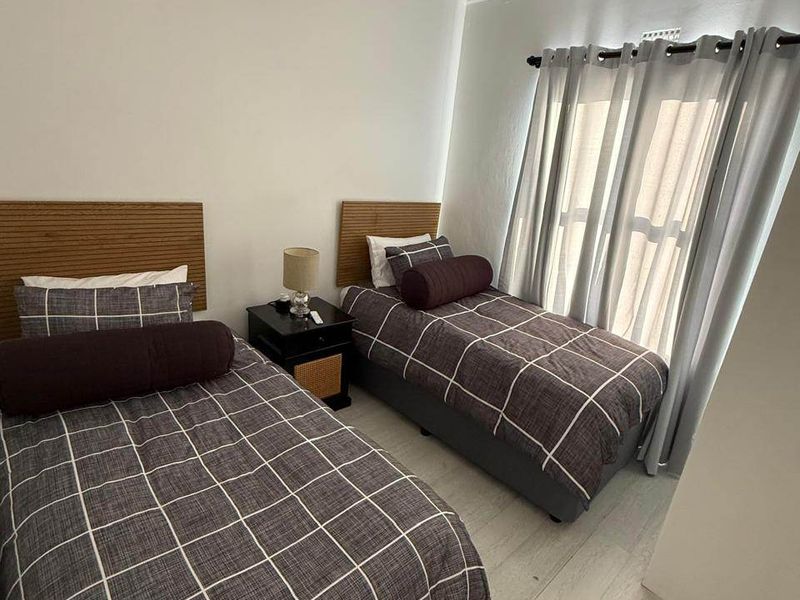 A well-maintained bedroom featuring light-toned laminate flooring, crisp white walls, and decorative ceiling cornicing, providing a clean and neutral living space.