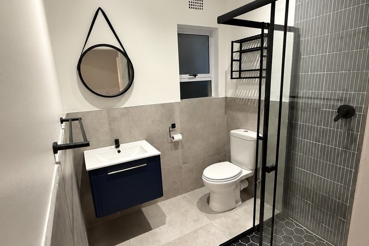 A modern, renovated bathroom featuring a wall-mounted vanity, walk-in shower with black frame, and contemporary grey tiling.