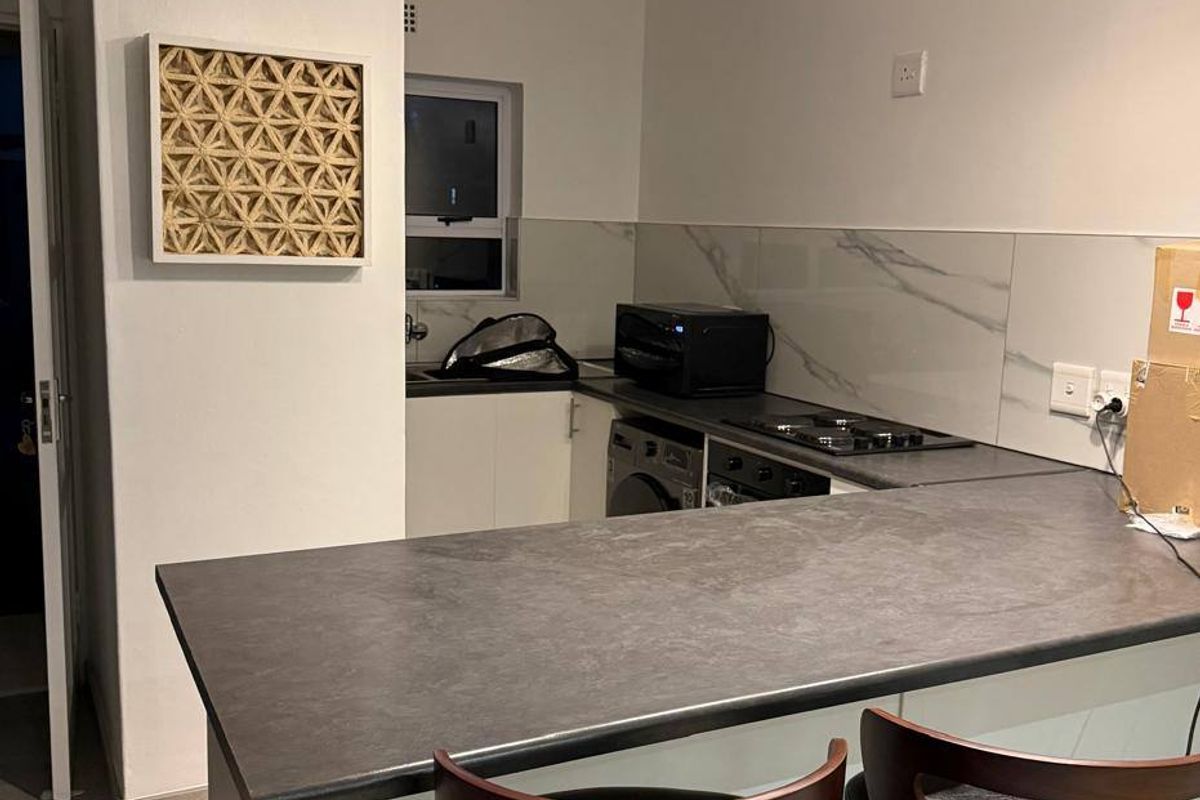 Modern kitchen featuring a breakfast bar, marble-effect splashback, built-in oven and hob, and contemporary pendant lighting.