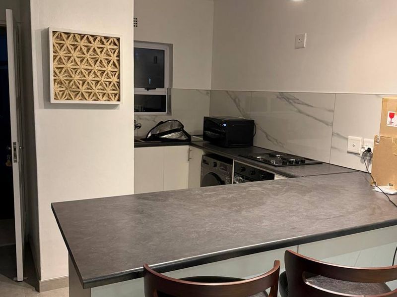 Modern kitchen featuring a breakfast bar, marble-effect splashback, built-in oven and hob, and contemporary pendant lighting.