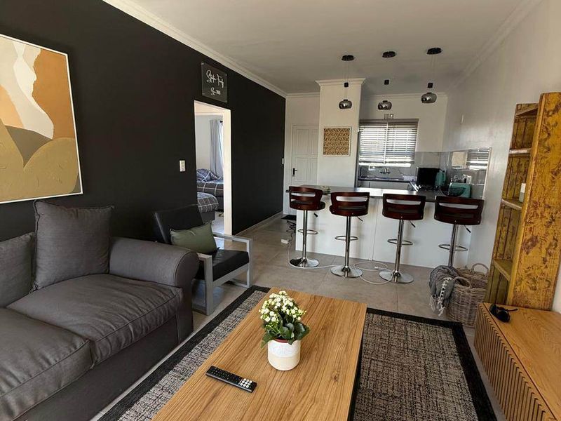 An open-plan living and kitchen area featuring a breakfast bar, tiled flooring, and modern recessed lighting, creating a functional and cohesive living space.