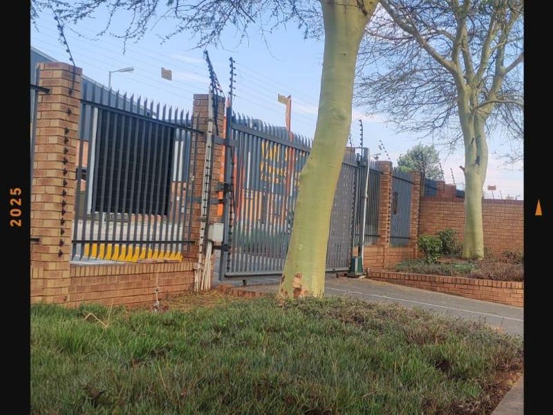 Front exterior view of the commercial property featuring a secure brick boundary wall, electric fencing, steel gate, and established garden landscaping.