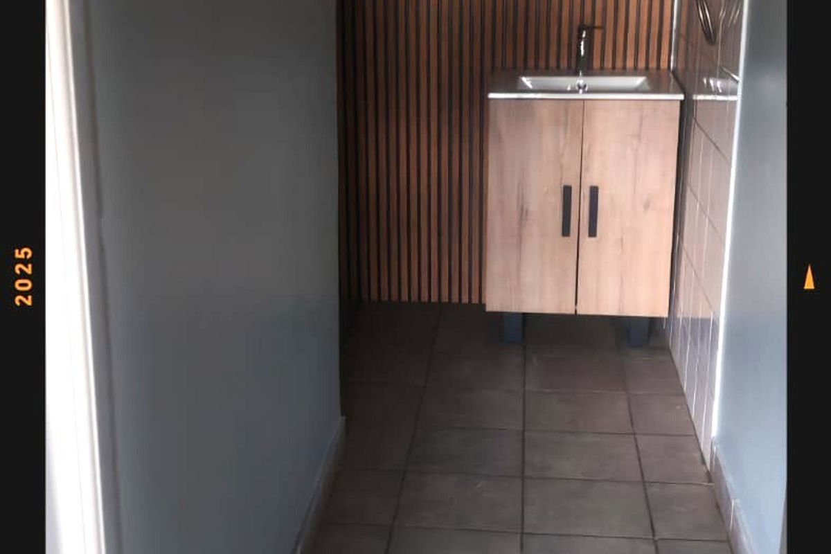 A compact commercial bathroom featuring a modern vanity unit, tiled flooring, and decorative slatted timber wall paneling.