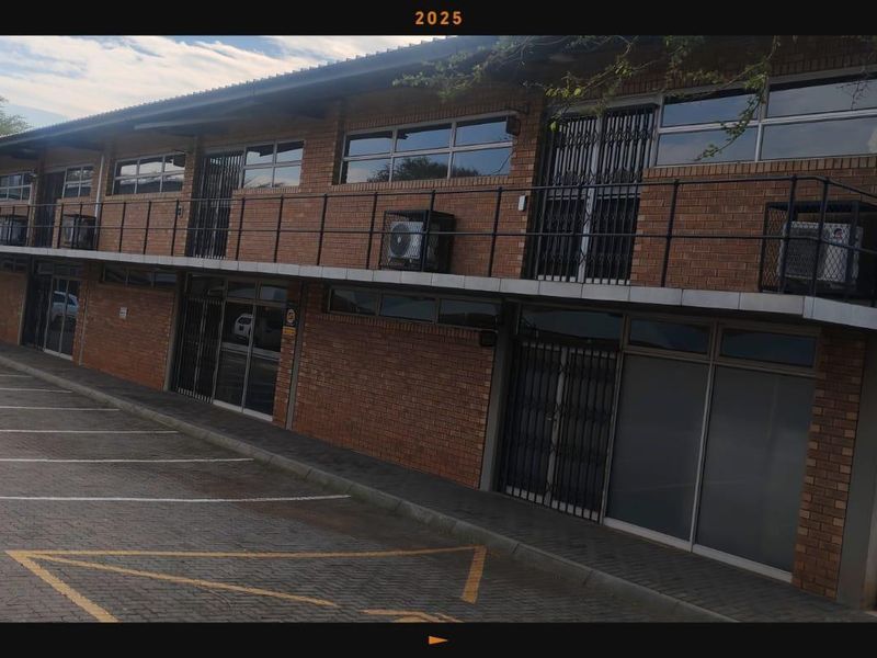 A multi-level commercial building featuring a face brick facade, external security gates, and dedicated paved parking spaces.